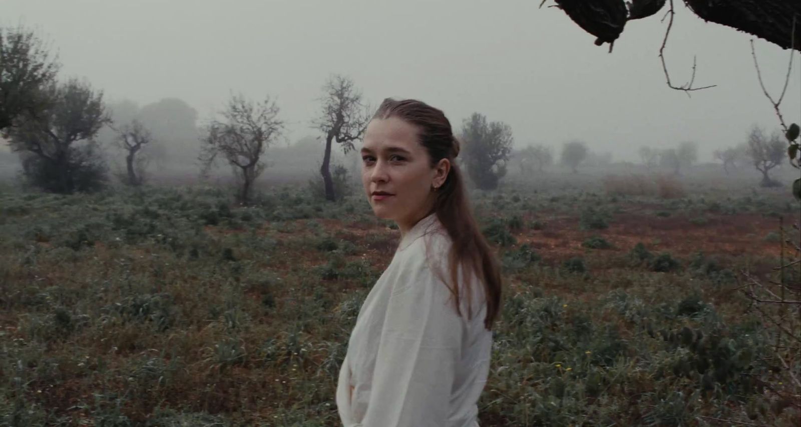 a woman standing in a field with trees in the background