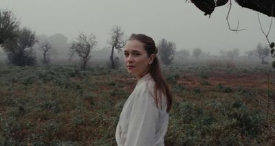 a woman standing in a field with trees in the background
