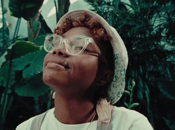 a woman wearing glasses and a hat in front of plants