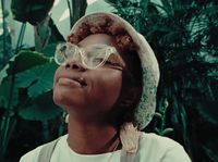 a woman wearing glasses and a hat in front of plants