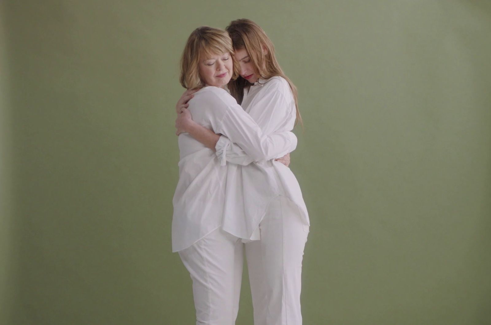 two women hugging each other in front of a green wall