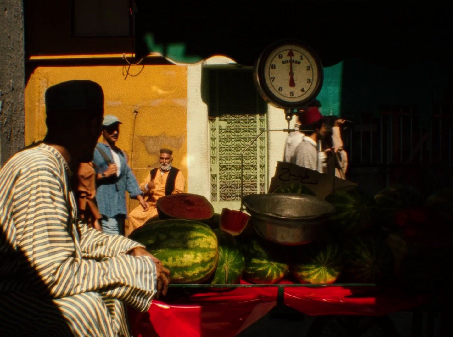 a man sitting in front of a pile of watermelon