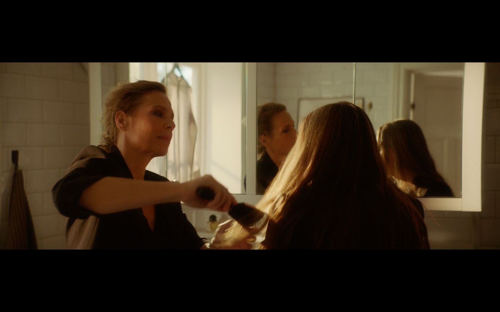 a woman blow drying another woman's hair in a bathroom