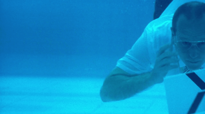 a man in a white shirt and sunglasses swimming in a pool