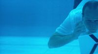 a man in a white shirt and sunglasses swimming in a pool