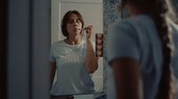 a woman standing in front of a mirror brushing her teeth