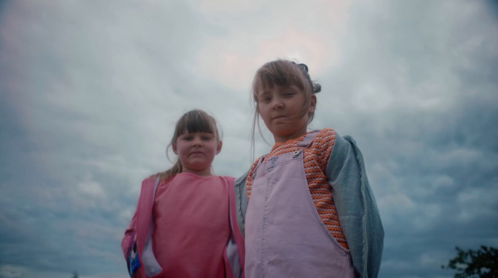 two young girls standing next to each other under a cloudy sky