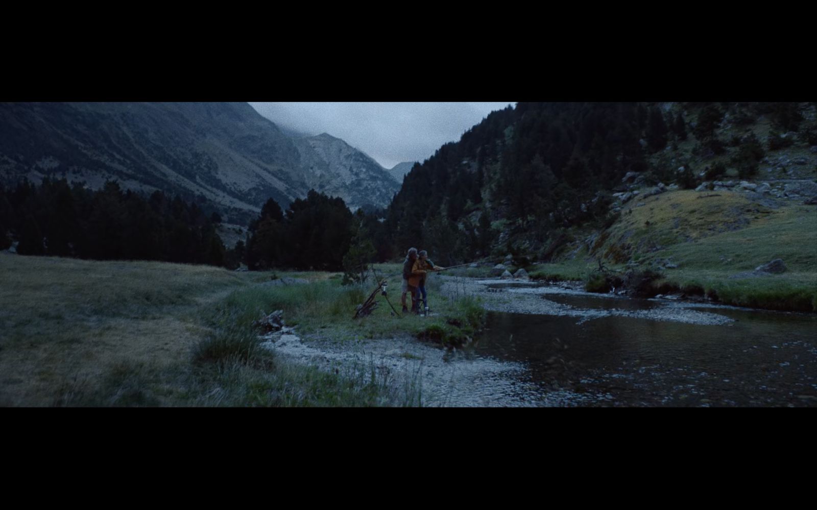 a man walking across a lush green field next to a river