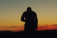 a silhouette of a man standing in front of a sunset