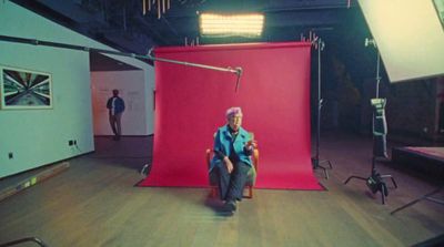 a man sitting in a chair in front of a red backdrop