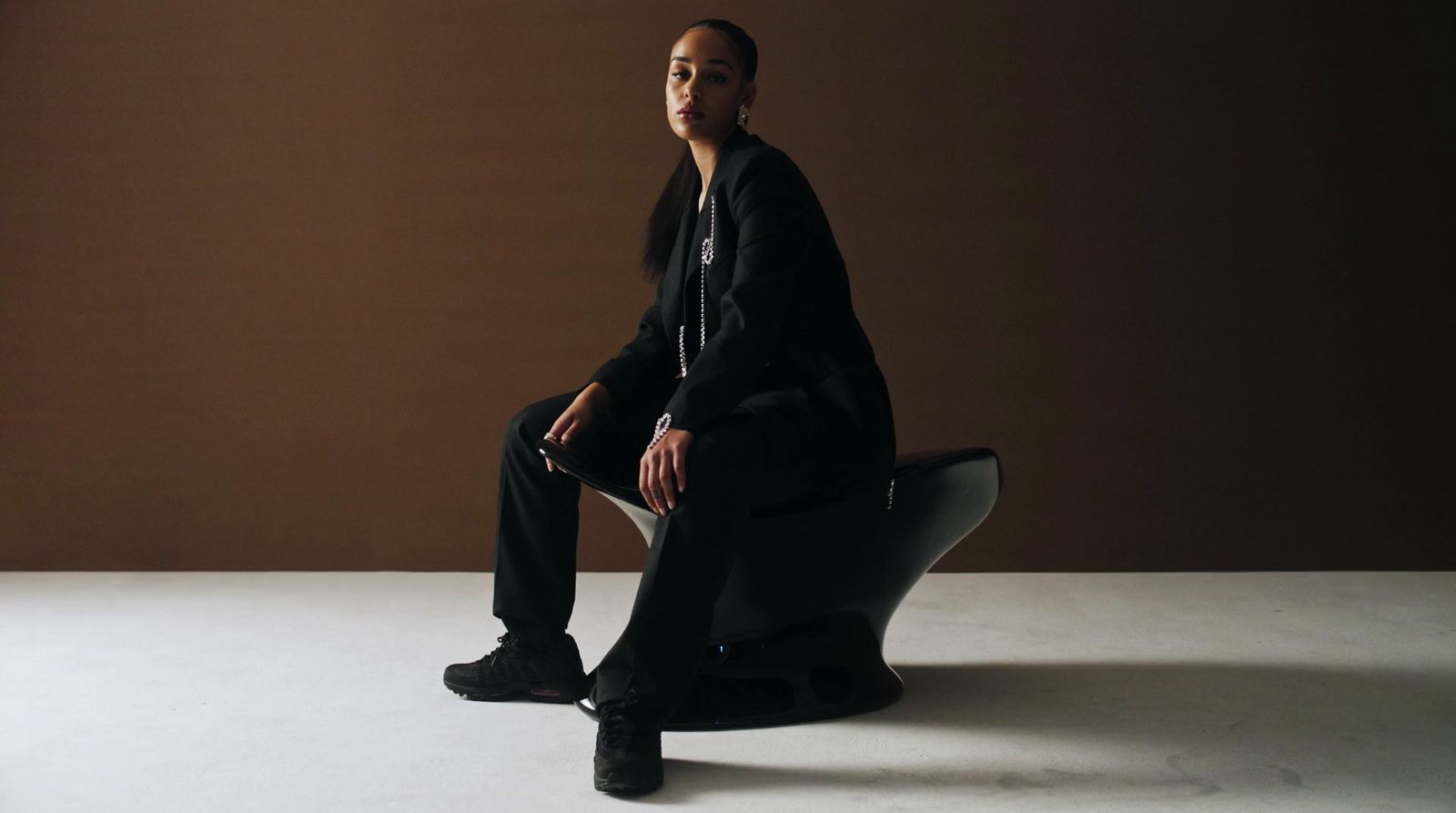 a woman sitting on top of a chair in front of a brown wall