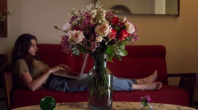 a woman sitting on a couch with a vase of flowers