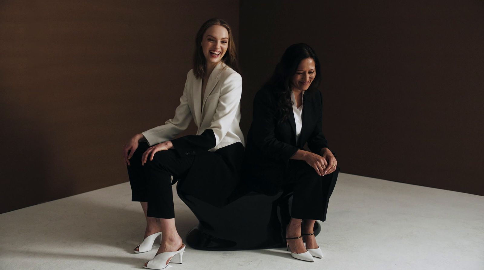 two women sitting next to each other on a white surface