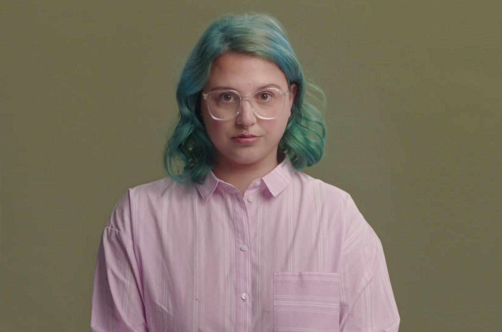 a woman with green hair wearing glasses and a pink shirt