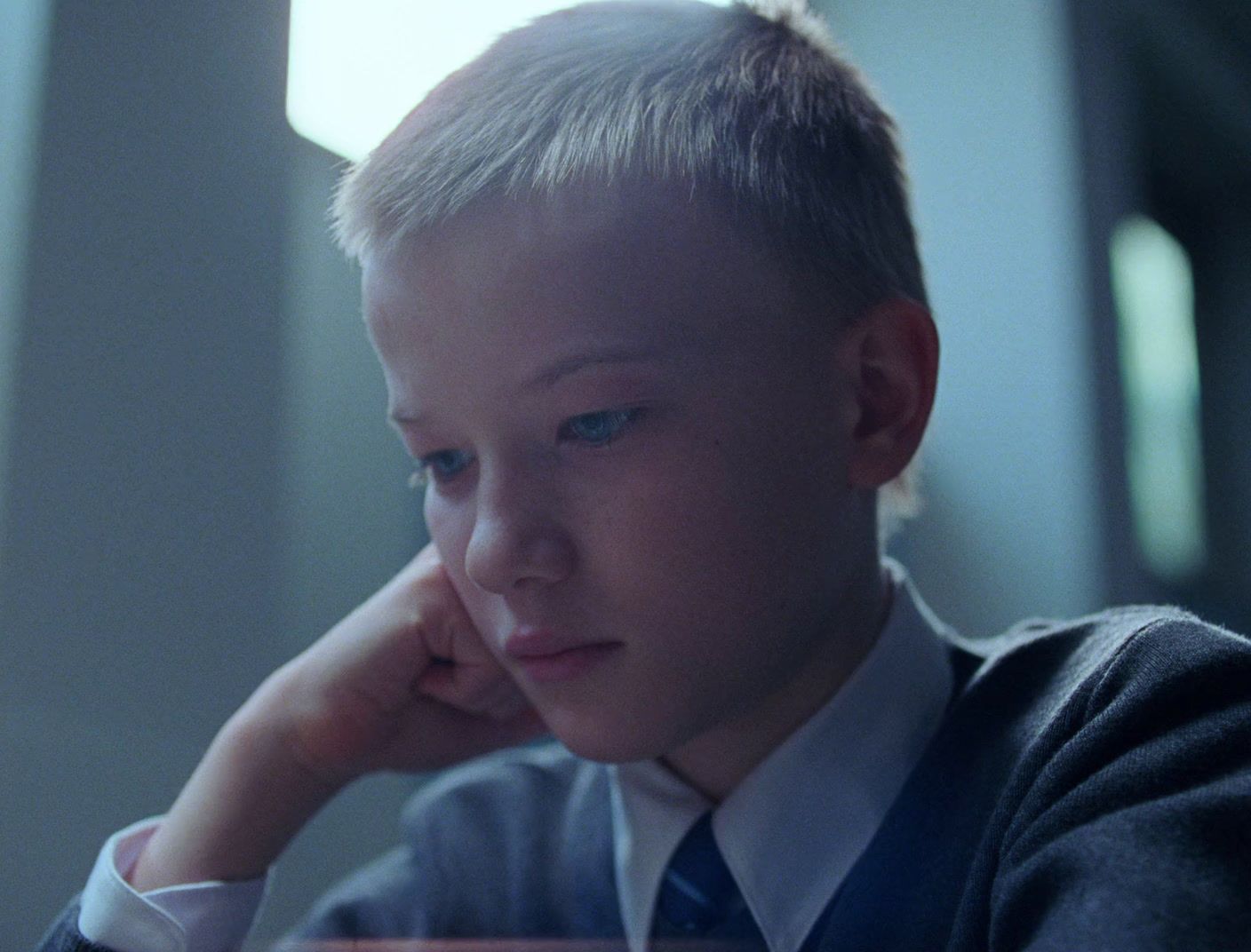 a young boy sitting at a table with his hand on his chin