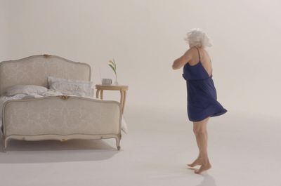 a woman in a blue dress standing in front of a bed