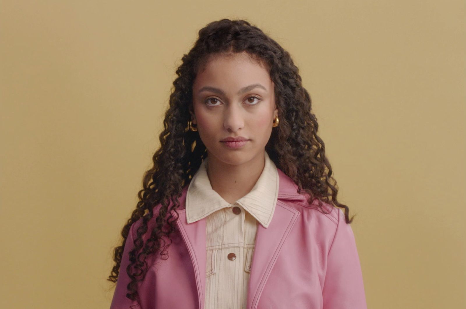 a young woman with curly hair wearing a pink coat