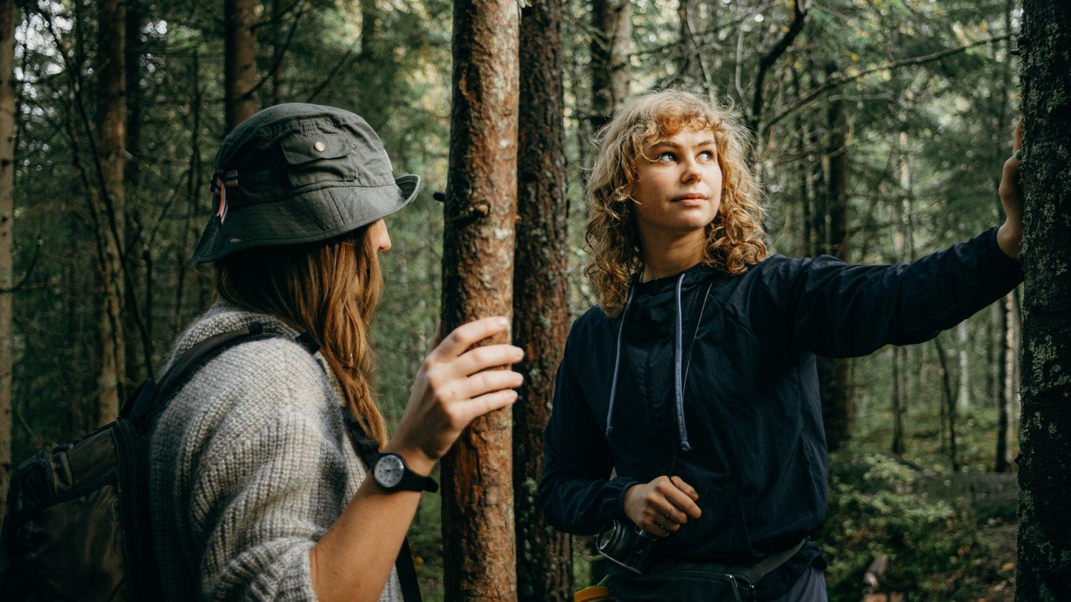 two women standing in the woods talking to each other