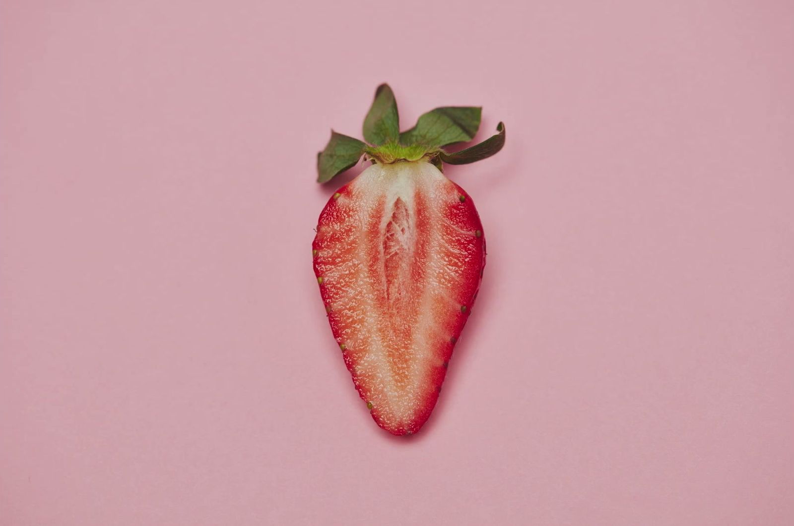 a strawberry cut in half on a pink background