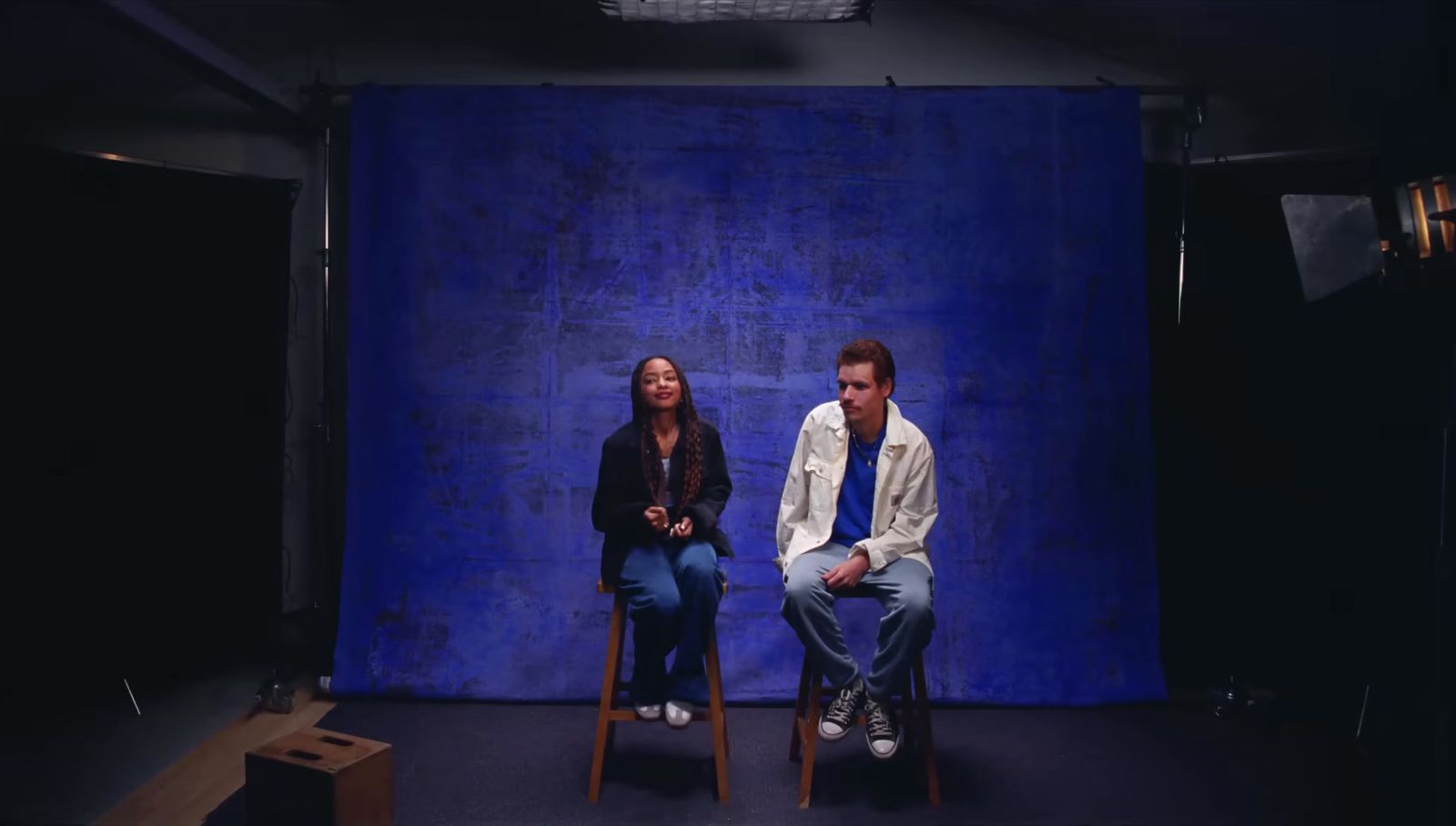 two people sitting on chairs in front of a blue backdrop