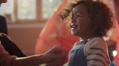 a little girl smiles as she holds her mother's hand