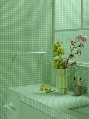 a green tiled bathroom with a vase of flowers