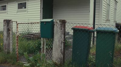 a house behind a chain link fence with a trash can in front of it