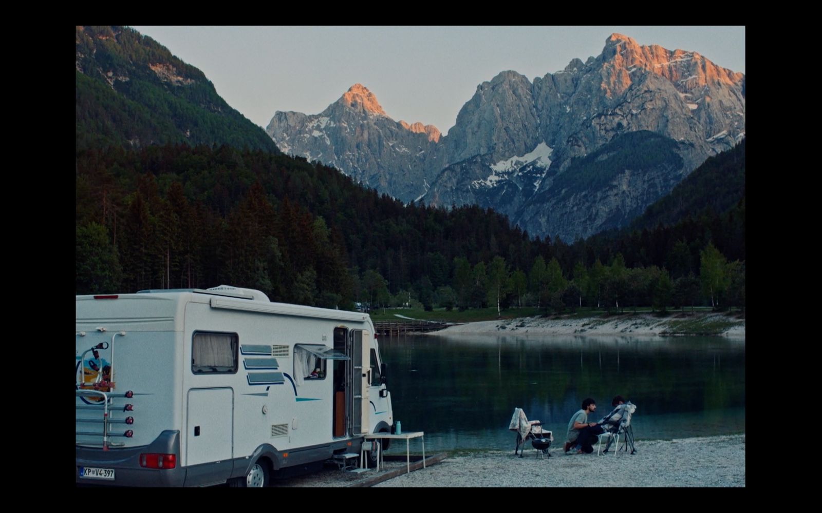 a camper parked next to a lake with mountains in the background