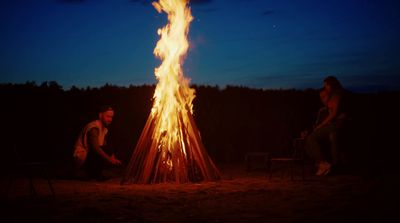 two people sitting around a campfire at night