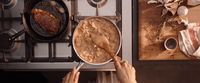 a person cooking food in a skillet on a stove