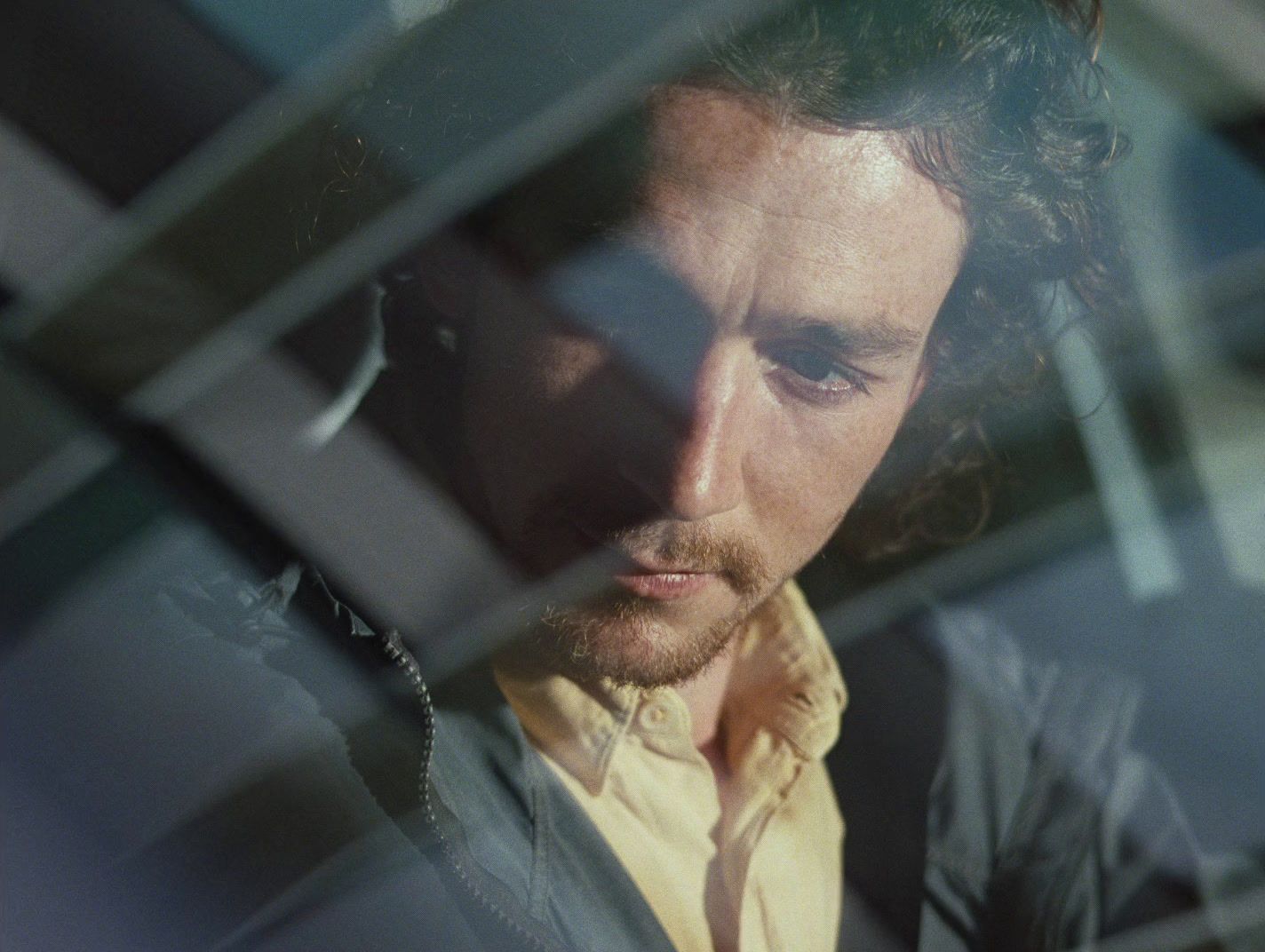 a man in a yellow shirt looking out of a window