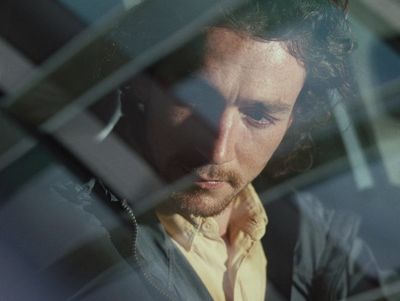 a man in a yellow shirt looking out of a window