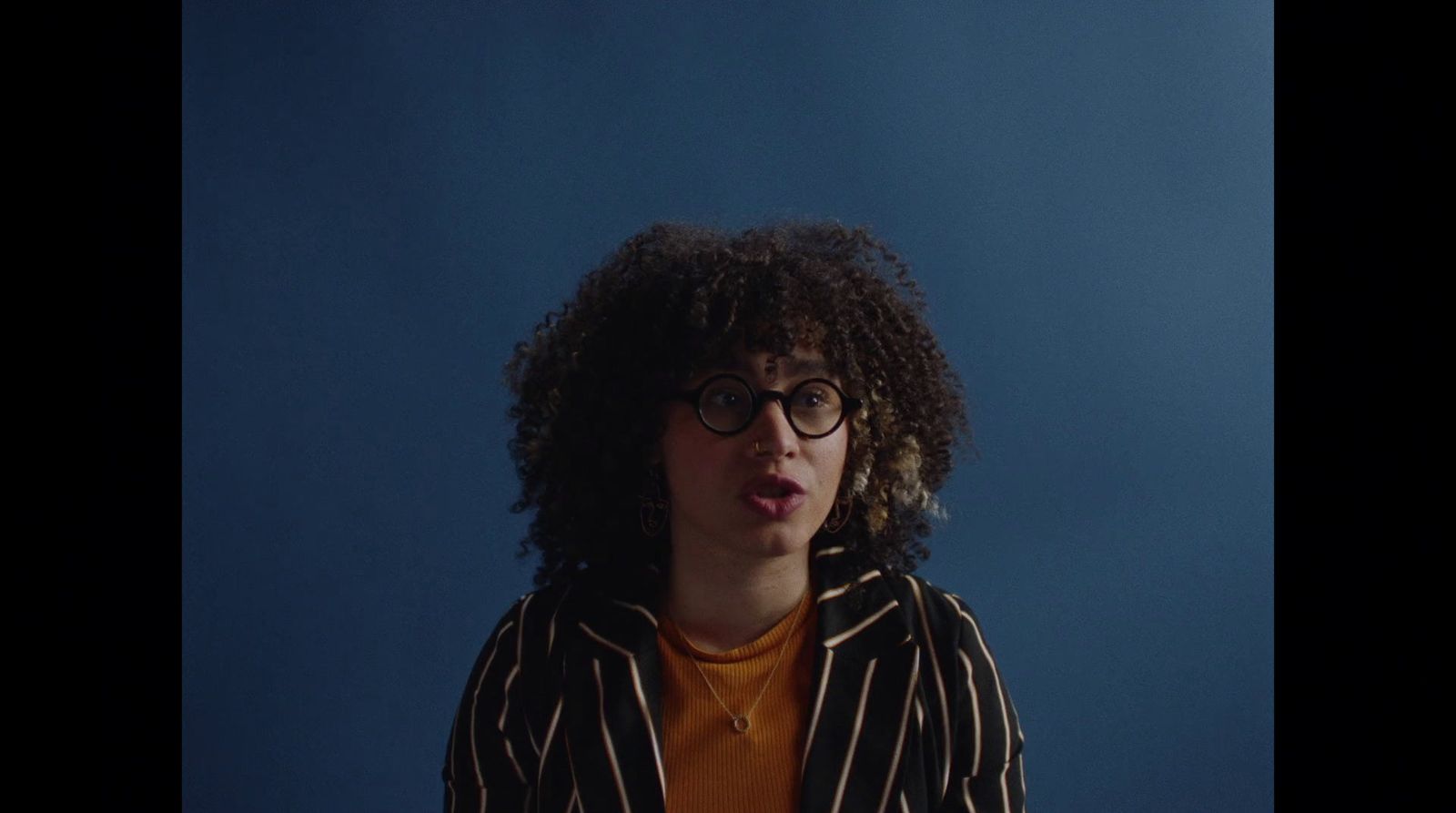 a man with curly hair and glasses making a funny face