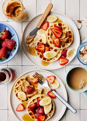 two plates of waffles with sliced bananas and strawberries