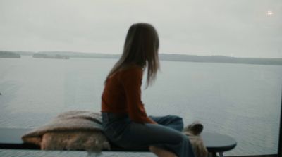 a woman sitting on a window sill looking out at a body of water