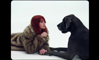 a woman in a fur coat sitting next to a black dog