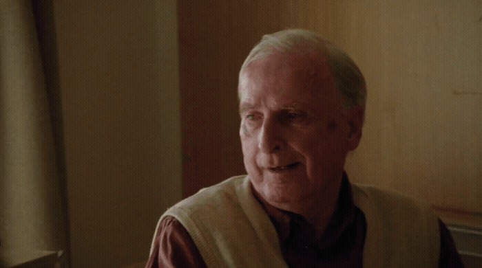 an older man wearing a vest and smiling
