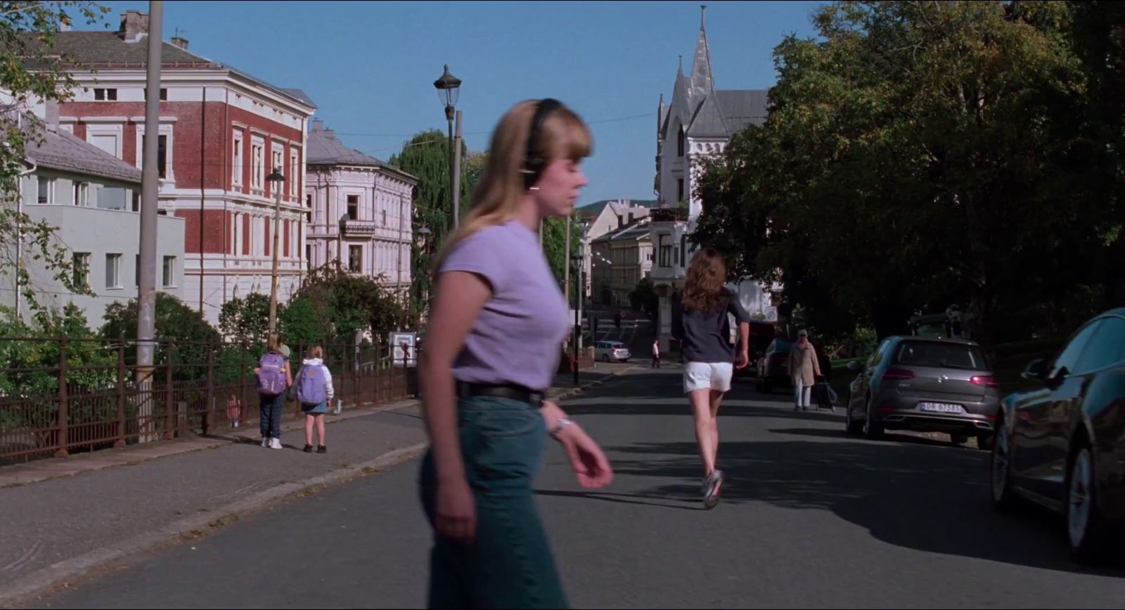 a woman walking down a street next to parked cars