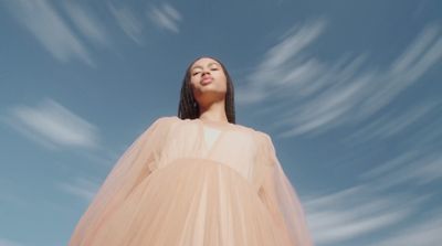 a woman with her eyes closed standing in front of a blue sky