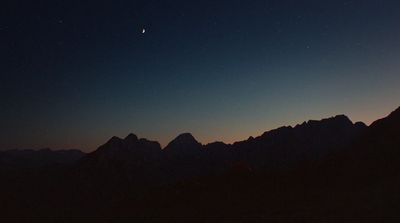 a night sky with the moon and stars above a mountain range