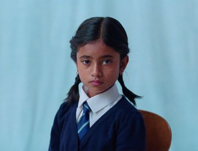 a young girl in a school uniform sitting in a chair