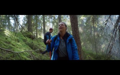 a woman in a blue jacket walking through a forest