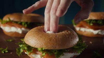 a hand reaching for a large sandwich on a table