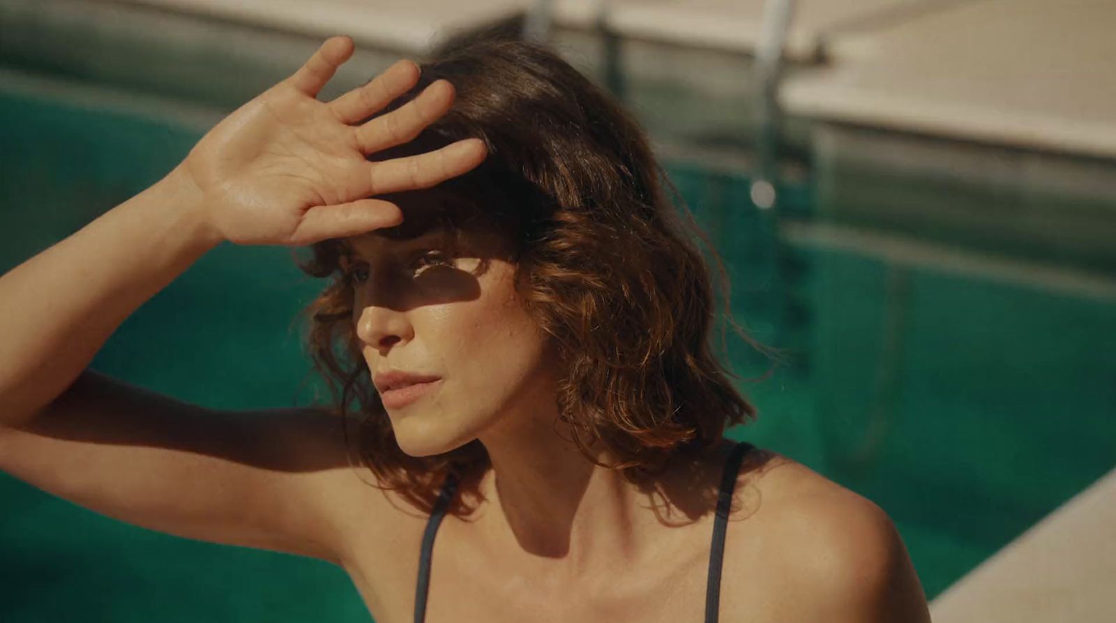 a woman in a bathing suit holding her hands to her head