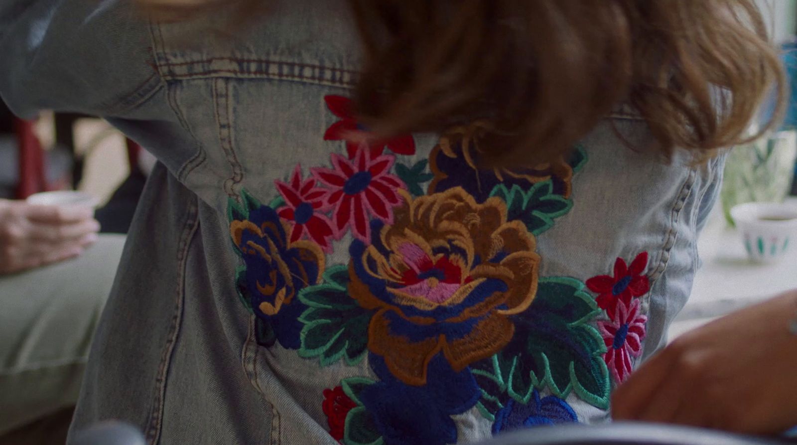 a woman wearing a jean jacket with flowers on it