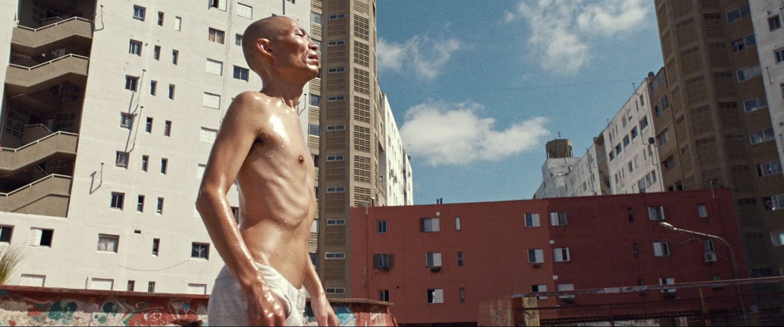 a man without a shirt standing in front of a tall building