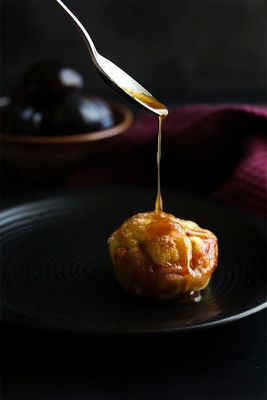 a spoon drizzling honey onto a pastry on a black plate