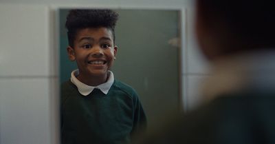 a young boy in a green sweater looking at himself in a mirror