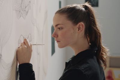 a woman drawing on a wall with a pencil