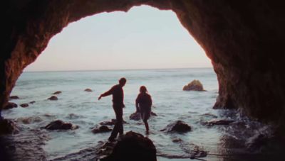 a couple of people standing in a cave near the ocean